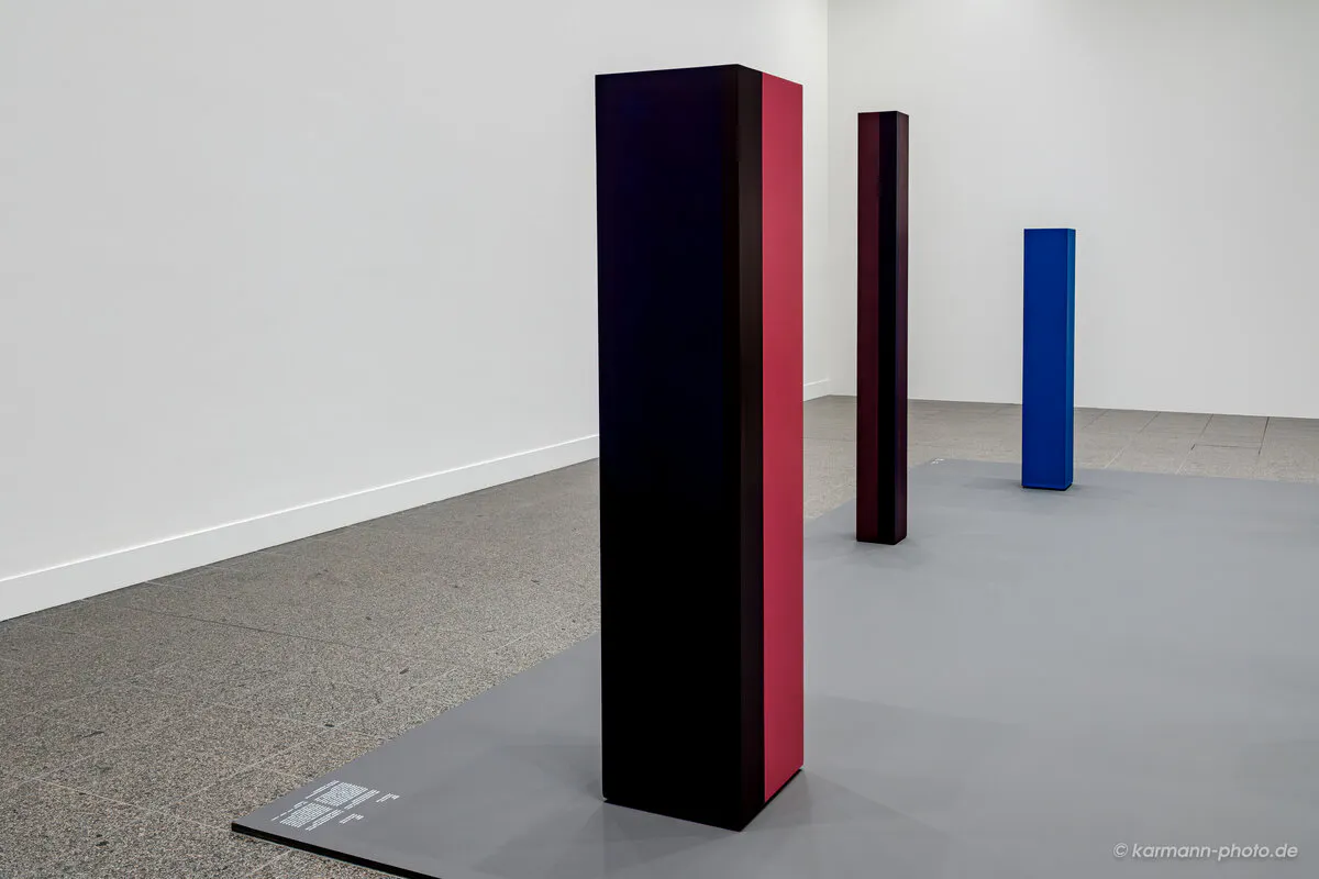 Kunstinstallation mit farbigen Säulen vor weißer Wand