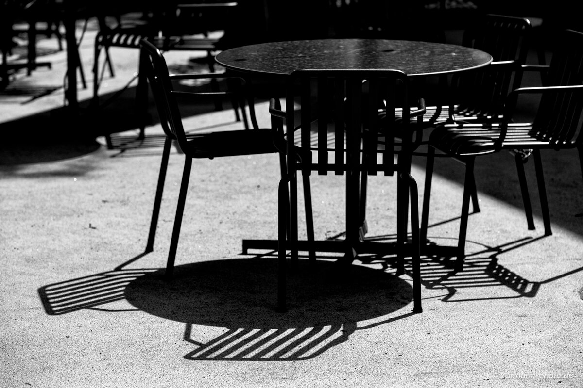 Schwarz-weiß Bild von Stühlen und Tisch im Sonnenlicht